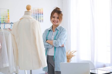 A professional fashion designer standing in her tailor shop with arms folded confident and looking at camera with a big smile. She is smiled with confident.