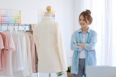 A professional fashion designer standing in her tailor shop with arms folded confident and looking at camera with a big smile. She is smiled with confident.