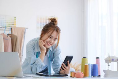 Fashion designer tailor is working in the design studio using laptop to checking customer order on online shop. Business owner, start up small business owner and online business concept.