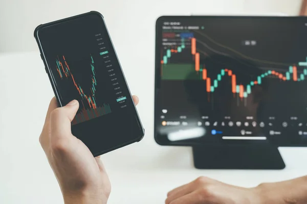 stock image Close-up of person's hands holding smartphone and tablet trading online on application, looking at screen, planning, and analyzing data to make decision. Online trading concept.