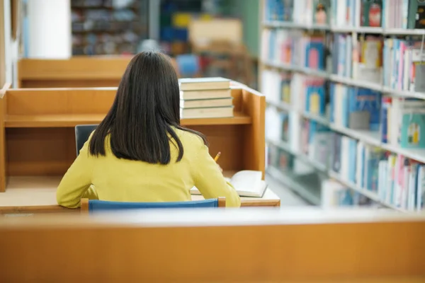 年轻的女大学生穿着休闲装坐在私人书桌前看书 并在图书馆为学校项目做研究 学习教育图书馆概念 — 图库照片