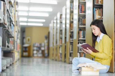 Yerlerde oturmuş kitap okuyan, bir kütüphanede okul projesi için araştırma yapan, günlük giysiler içinde genç bir üniversite öğrencisi. Öğrenim, Eğitim, Kütüphane konsepti.