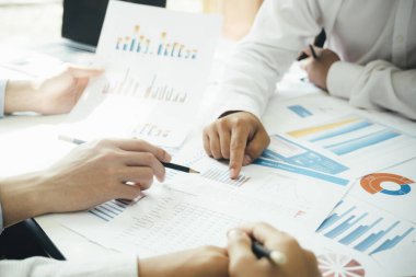 İş yerinde birlikte çalışan iş adamlarının yakın çekimleri, stratejiler, planlar, analitik ilerleme ve finansal istatistikler hakkında tartışmaları ve masa başındaki kalem tutan grafik belgelerine işaret etmeleri. İş ve