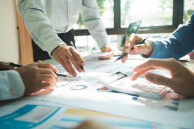 İş yerinde birlikte çalışan iş adamlarının yakın çekimleri, stratejiler, planlar, analitik ilerleme ve finansal istatistikler hakkında tartışmaları, ve masa başındaki kalem ve hesap makinesi tutan grafik belgelerine işaret etmeleri. İş ve Takım Çalışması konsepti.