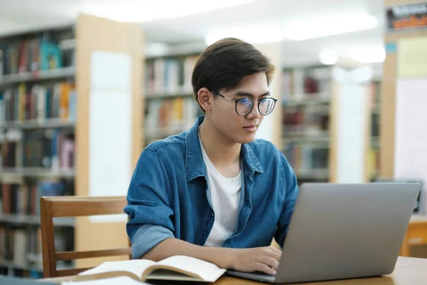 안경을 책상에 연구나 과제에 정보를 검색하기 도서관에서 노트북을 사용하여 공부하고 — 스톡 사진