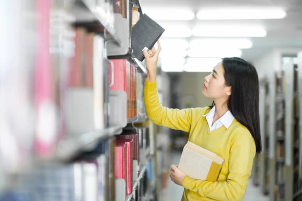 穿着休闲装的年轻亚洲女学生站着 寻找和选择在图书馆读书 学术研究或学校工作或项目的书籍 图书馆概念 — 图库照片