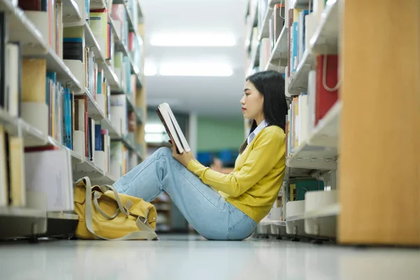 身着休闲装的女大学生坐在地板上看书 为图书馆的学校项目学习和做研究 图书馆概念 — 图库照片