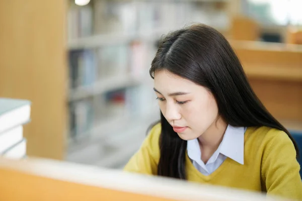 年轻的女大学生穿着休闲装坐在私人书桌前看书 并在图书馆为学校项目做研究 学习教育图书馆概念 — 图库照片