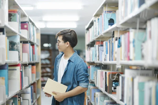 学術研究や学校の仕事を勉強するために図書館で読む本を探して選択し バックパック立ってカジュアルな服装の若い男性学生 教育の概念 — ストック写真
