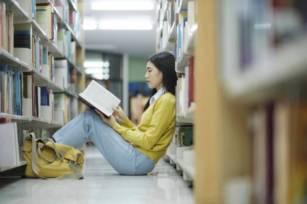 身着休闲装的女大学生坐在地板上看书 为图书馆的学校项目学习和做研究 图书馆概念 — 图库照片