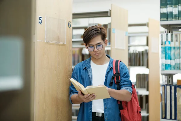 学術研究や学校の仕事を勉強するために図書館で読むために バックパックの立って 読書や選択本を持つカジュアルな服装の若い男性学生 教育の概念 — ストック写真