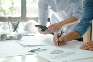 Birlikte çalışan iki mühendis, geliştirici ya da mimarın yakın plan çekimleri, yapım projesinin grafik tasarımı, hesap makinesi, ve kağıtlarla birlikte çalışma masasında gelişim için tartışmalar