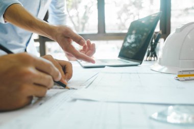 Birlikte çalışan iki mühendis, geliştirici ya da mimarın yakın plan çekimleri, inşaat projesinin grafik tasarımı, kağıtlar ve diğer şeylerle birlikte çalışma masasında gelişim için işaret etmek ve tartışmak.