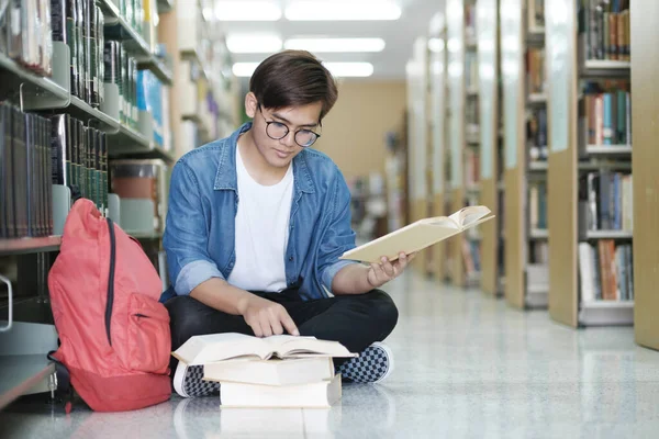 本を読み 図書館で学校のプロジェクトのために勉強し 研究を行う床に座って眼鏡やカジュアルな服を着て若い男性の大学生 学びと教育の概念 — ストック写真