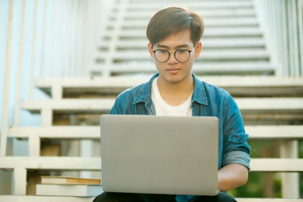 年轻的男大学生戴着眼镜 穿着休闲装 笑着坐在楼梯上 用笔记本电脑学习 为学校的项目和研究寻找信息 教育和教育 — 图库照片