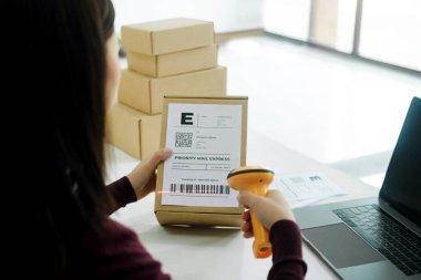 Genç bayan internet işletme sahibini kapatın. Girişimci elinde dizüstü bilgisayarla kargo etiketi üzerinde barkod taraması yapıyor. Karton kutu teslimattan önce ya da müşteriye teslim edilmeden önce. Çevrimiçi