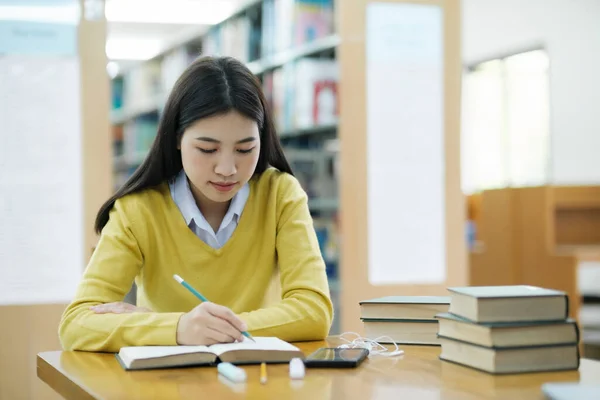 身着休闲装的女大学生坐在课桌前学习 并独自在图书馆为研究或学校项目写作 电子学习教育图书馆概念 — 图库照片