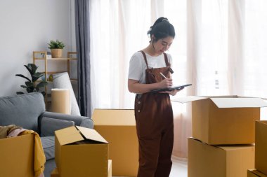 Karton kutuları kontrol eden ve paketleyen Asyalı kadın, kontrol listesiyle çevrimiçi alışveriş yapan müşterilere teslim edilmeden önce yeni ev taşıma, nakliye veya ürün paketlerini kontrol etmeye hazır olun.