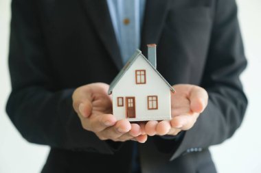 Emlakçı bir ev modeli tutuyor ve müşteriye bazı tavsiyelerde bulunuyor. Ev konsept sigortası hırsızlık veya yıkım için koruma programını teşvik etmektir..