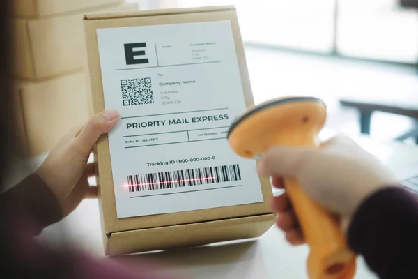 Close up of young female online business owner, entrepreneur sitting at desk scanning barcode on shipping label of parcel, cardboard box before shipment or delivery to customer. Online business, e
