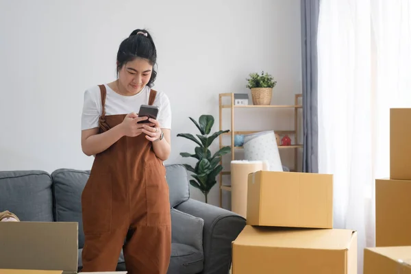 Young single woman using her mobilephone to checking list stuff and contract with moving house service.