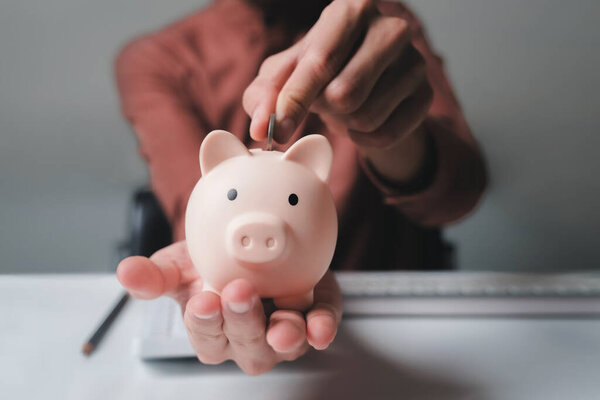 Close up of businessman hands holding and putting coin into piggy bank on hand for saving, planning and calculating financial plans and strategies for the growth of business, investment, and