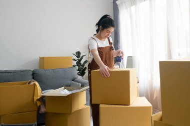 Yeni eve taşınırken, bir sürü karton kutunun arasında eşyalar paketleyen mutlu bekar bir kadın. Yalnız yaşamak. Modern kadın insanlar evlerine taşınıyor. Ev içinde boş zaman aktivitesi.