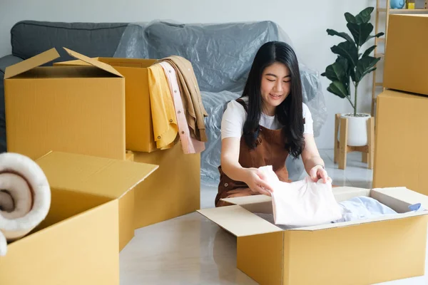 Happy single young woman packing or unpacking cardboard boxes while moving to new house or new apartment. New beginnings emotion. Living alone. Modern female people in moving home apartment leisure