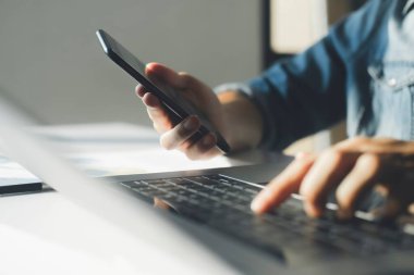 Close up of businessman is analyzing investment data by look at laptop and mobile phone that have online graphs and diagrams. He is checking financial report presentation.