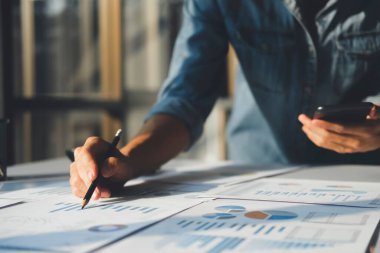 İş adamlarına yakın plan, çevrimiçi grafik ve diyagramları olan cep telefonlarına bakarak yatırım verilerini analiz ediyor. Mali rapor sunumunu kontrol ediyor..