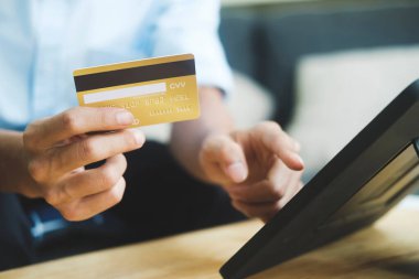 Genç bir işadamı kredi kartını tutuyor ve evde dizüstü bilgisayar kullanıyor. İnternetten alışveriş yapıyor ve faturaları ödüyor. Ödeme yöntemi:.