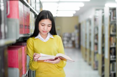 Ayakta duran, okumak ya da okumak için kütüphanede kitap seçen akademik araştırma, okul ödevi, proje ya da sınav yapan genç bir üniversite öğrencisi. Öğrenme, Eğitim