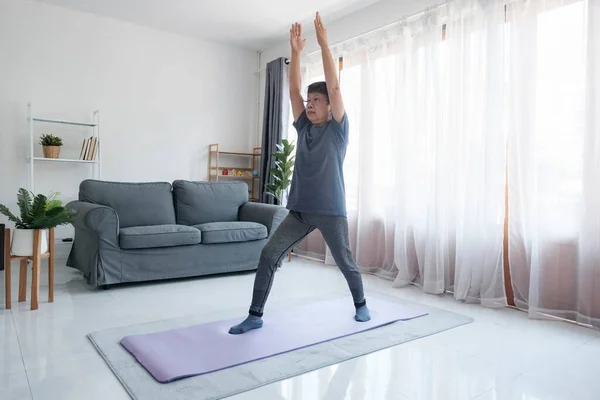 Healthy lifestyle and aging concept. Balance in life. Senior woman doing stretching exercise yoga in living room at home.