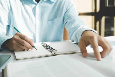 Kapanış öğrencisi çalışma masasındaki fotokopi kitabında kompozisyon yazıyor, notlar alıyor, açık kitaptan özet çıkarıyor, okul yapıyor, ev ödevi yapıyor, araştırma çalışması yapıyor.