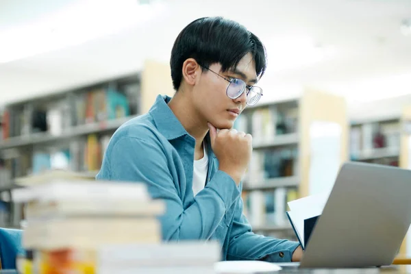 University Library: Smart asian university student uses Laptop, Writes Notes for Paper, Essay, Study for class assignment. Focused students learning, studying for college exams.