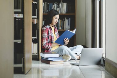 Üniversite Kütüphanesi: Güzel, zeki Asyalı üniversite öğrencisi Laptop kullanır, Kağıt için Notlar Yazar, Sınıf ödevi için Çalışma. Odaklanmış öğrenciler öğreniyor, üniversite sınavlarına çalışıyor..