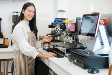 Modern bir kahve dükkanında otomatik bir makinede kahve hazırlarken önlük giyen neşeli genç barista. Ticari mülkiyet kavramı.