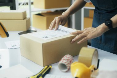 Genç bayan çevrimiçi iş sahibinin masa başında dizüstü bilgisayar ve kutularla oturup karton kutulara ya da teslimat ve teslimat için hazırlanan müşteri paketlerine nakliye etiketi koymasını kapatın..