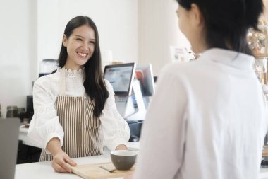 Kahve dükkanının sahibi, mühürlü kahve fincanını bir müşteriye veriyor. Kahve dükkanında müşteriye gülümseyen bir kadın. Kahve dükkanında müşteriye kahve servisi yapan güler yüzlü bir barista.