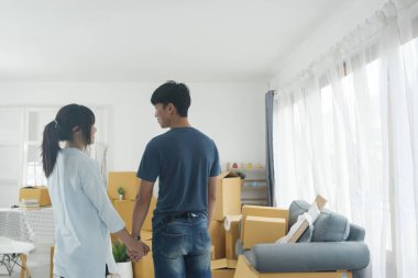 Asyalı genç mutlu evli çift yeni evlerine ya da gayrimenkullerine taşınıyor. Çekici romantik bir erkek ve kadın, içinde mutluluk ve sevgi olan kutular taşır. Aile taşınma konsepti.