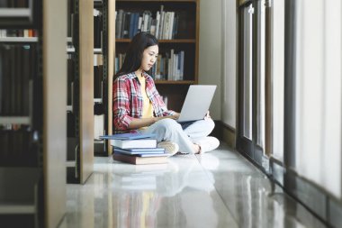 Üniversite Kütüphanesi: Güzel, zeki Asyalı üniversite öğrencisi Laptop kullanır, Kağıt için Notlar Yazar, Sınıf ödevi için Çalışma. Odaklanmış öğrenciler öğreniyor, üniversite sınavlarına çalışıyor..