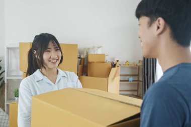 Asyalı genç mutlu evli çift yeni evlerine ya da gayrimenkullerine taşınıyor. Çekici romantik bir erkek ve kadın, içinde mutluluk ve sevgi olan kutular taşır. Aile taşınma konsepti.