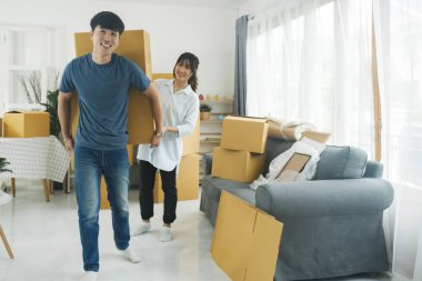 Asian young happy new married couple moving to their new house or real estate. An attractive romantic man and woman carry boxes parcel with happiness and love. Family moving house relocation concept. clipart