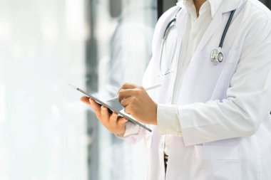 Dijital tablet kullanan bir doktorun görüntüsü. Klinikte dijital tablet kullanan doktorların ellerini kapatın. İşçi ceketli ve steteskoplu doktorun dijital tablet tutuşu. Doktor üzerinde çalışıyor.