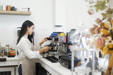 Modern bir kahve dükkanında otomatik bir makinede kahve hazırlarken önlük giyen neşeli genç barista. Ticari mülkiyet kavramı.