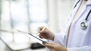 Dijital tablet kullanan bir doktorun görüntüsü. Klinikte dijital tablet kullanan doktorların ellerini kapatın. İşçi ceketli ve steteskoplu doktorun dijital tablet tutuşu. Doktor üzerinde çalışıyor.