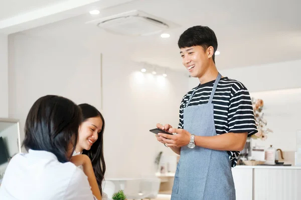 Cheerful smiling waiter in apron using table while take order and talk to clients cafe coffee shop visitors, friendly professional man server wear apron write menu choice, serving staff good customer