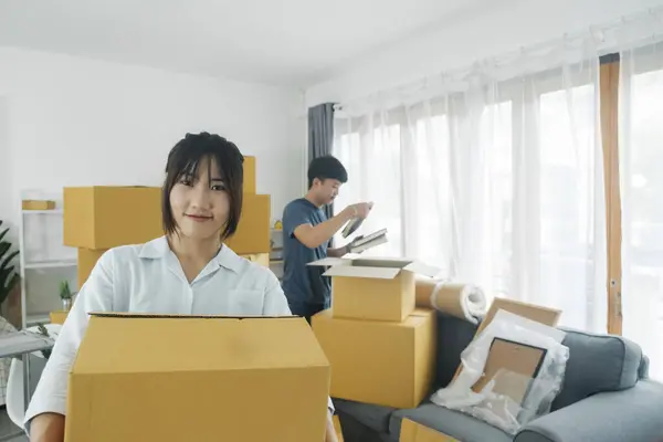 Asian young happy new married couple moving to their new house or real estate. An attractive romantic man and woman carry boxes parcel with happiness and love. Family moving house relocation concept.