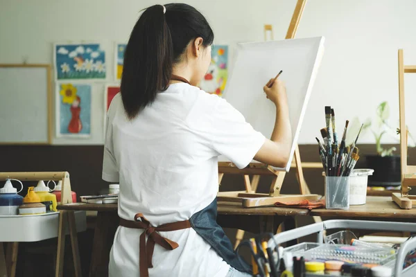 年轻的女画家在工作室的画布上画或画她的画 一个喜欢艺术和绘画的少女正在花些时间在画布上创作她的水彩画 — 图库照片