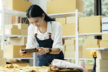 İnternette satmak ve paket ürün kutusu hazırlamak için cep telefonu veya akıllı telefon dijital kamerasıyla fotoğraf çeken genç kadınlar. Çevrimiçi fikirler satmak. Genç kadın.